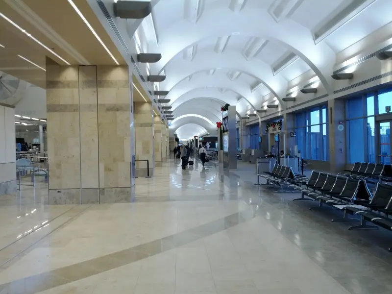 The vaulted gate concourse of Terminal C at John Wayne Airport, with holiday garlands and a few travelers pulling bags