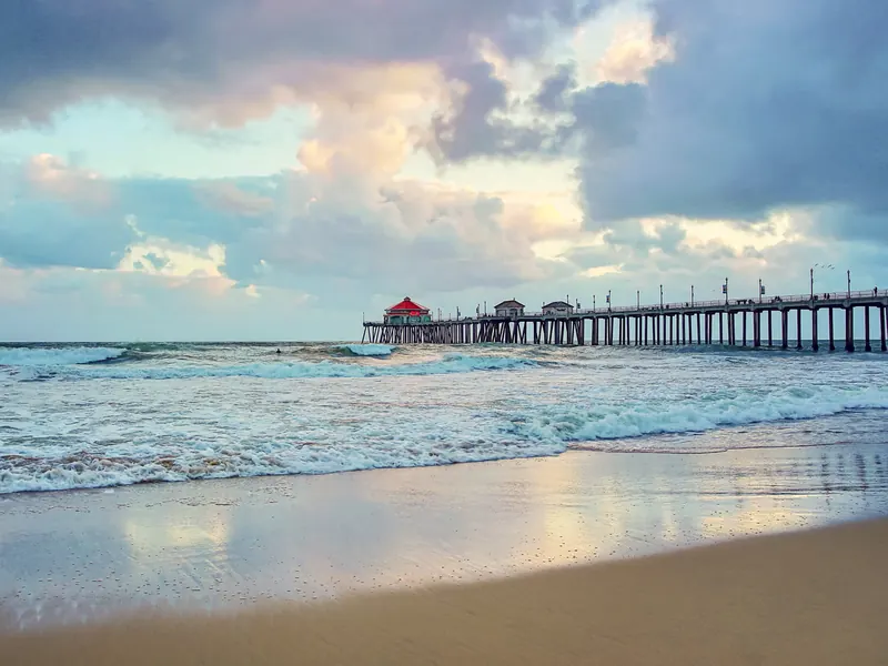 Storm clouds over the Huntington Beach Pier, with surf rolling onto wet sand